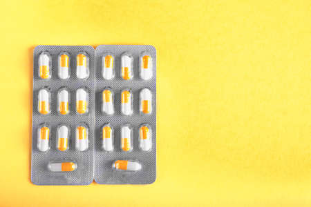 Pills on a light yellow background. Two bright packs of medical capsules. Orange and white drugs. Painkillers and antibiotics in blisters. Prescripted medicine.の写真素材