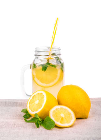 Lemon slices and long, straight and thin yellow straw in a large jar with mojito. A big glass jug with lemon juice and yellow lemons on a light fabric, isolated on a white background.の写真素材