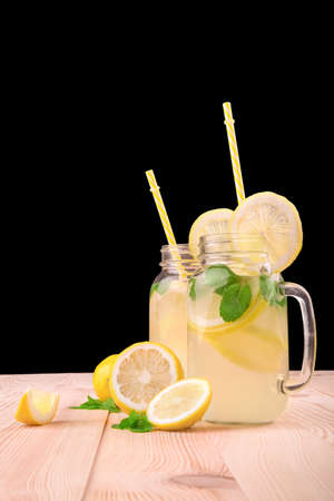 Healthy organic lemonade beverages in two huge transparent mson jars and with cute yellow straws and ripe lemons, bright green limes and fresh mint on a black background, close-up.の写真素材