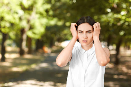 A gorgeous woman in an elegant blouse on a natural background. A concerned girl is holding her head in disappointment. A nice girl standing in a green park. Business lady in a white shirt on nature.の写真素材