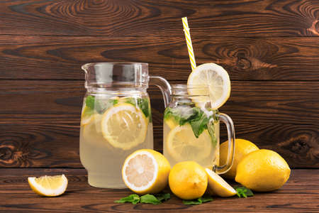 A pitcher and a glass of a tasty and refreshing mojito from green mint and ripe yellow lemons on a dark wooden background. Cold tea with lemon and mint on a wooden background.の写真素材