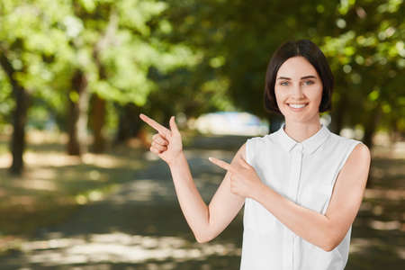 A portrait of a pretty girl in a white blouse outdoors. A confident girl posing in a big summer park. A Beautiful young business woman looks happy. A happy healthy lady on a natural background.の写真素材