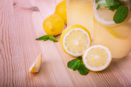 A lot of fresh and ripe yellow lemons with tasty and green mint leaves and two large transparent glasses with a refreshing summer drink made from citrus fruits, fresh leaves of mint and ice cubes.の写真素材