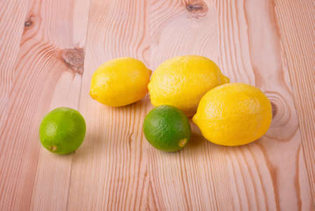 Three juicy, ripe and yellow lemons and two bright green limes. Tropic fruit. Lemons and limes on a light wooden table. Citrus fruits. Vitamins.の写真素材