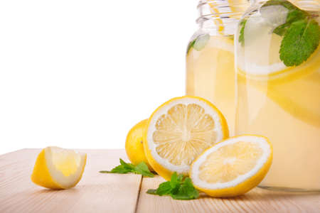 A lot of yellow lemons with tasty mint leaves and two huge glasses of cold lemonade drinks from citrus fruits, fresh leaves of mint and water on a light wooden table, isolated on a white background.の写真素材