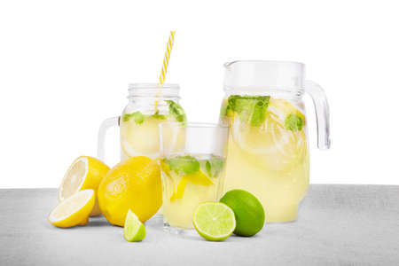 A glass, a mason jar and a jug  of summer mojito beverages from mineral water, bright yellow lemons with tasty leaves of mint on a light fabric, isolated on a white background. Refreshment.の写真素材