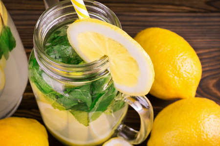 A top view of a mason jug of healthy organic lemonade with fresh lemon, lime, and mint on a dark brown wooden background. A refreshing lemonade with fresh lemons and bright green mint.の写真素材