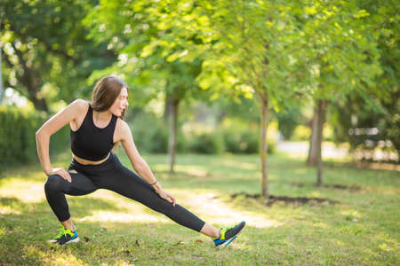 Beautiful, slim and charming sporty girl doing stretching in the large green park in the morning....