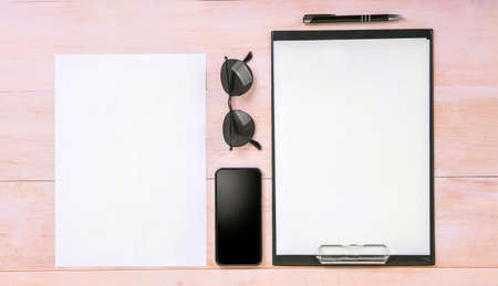 Great composition in a business style. Vector A4 format with a thin black pen, a big black smartphone, glasses on a light brown wooden table. The sheet of A4 paper near to other items.の写真素材