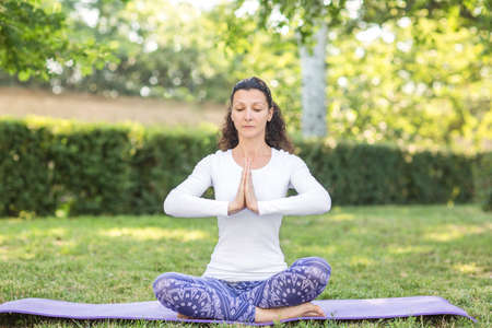 A girl is looking healthy, sporty and doing physical exercise. A beautiful sports lady is dressed in a white sweater and blue leggings. A charming sportswoman is sitting on the legs and holding her hands in front of hers.の写真素材
