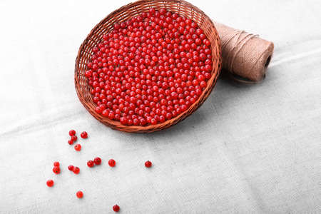 Ripe raw red currant in a basket. A light brown wooden basket with a beige coil of a thread on a fabric background. Healthful tasty currant for nutritious breakfast. Juicy berries.の写真素材