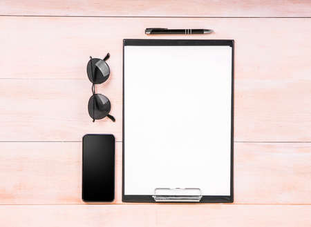 White clean sheets of paper with a thin black pen, a big black smartphone, glasses on a light brown wooden table.の写真素材