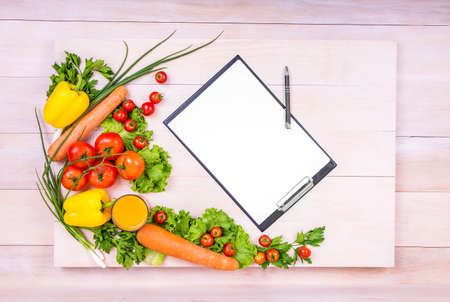 A spacious bright table with sheets of paper and a pen on it. A variety of tasteful vegetables. Healthful vitamins on a light background. Organic ingredients: tomatoes, lettuce, carrots, peppers.の写真素材