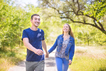 Wonderful young fall-in-love couple walking in the park. The young man and his girlfriend are smiling and happy together. Portrait of a beautiful, elegant and loving couple.の写真素材