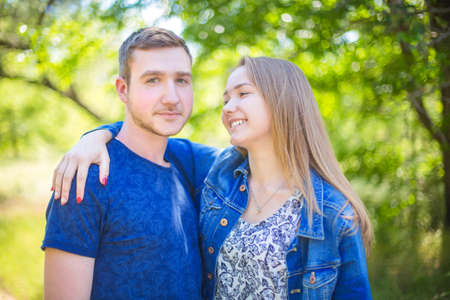 Incredible and fall-in-love couple in wonderful clothes in bright blue color are walking in the park. Romantic date from loving people. A good-looking girl is looking at her boyfriend and smiling.の写真素材
