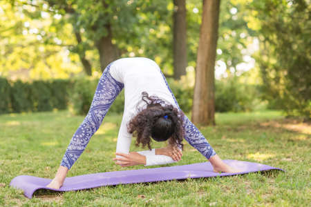 Young attractive woman practicing yoga at the nature background. The beautiful woman does yoga and looks healthy, perfectly and charming. The sports exercises have good benefits for health.の写真素材