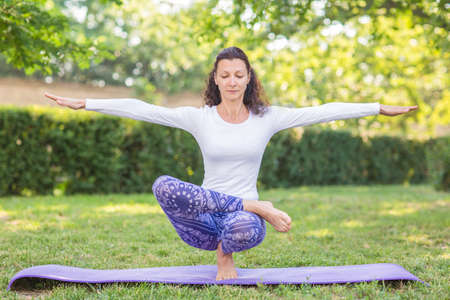 A slender girl is looking beautiful and athletic and doing physical exercise. A well-looking sports lady in a white sweater and leggings. A beautiful sportswoman issitting on one leg and spreading her hands to the sides.の写真素材