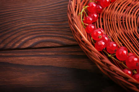 A colorful partial composition of a brown basket with juicy red currant on a dark brown wooden table. Mature, juicy, raw, fresh, tasty, healthy, nutritious concept. Delicious bright red currant.の写真素材