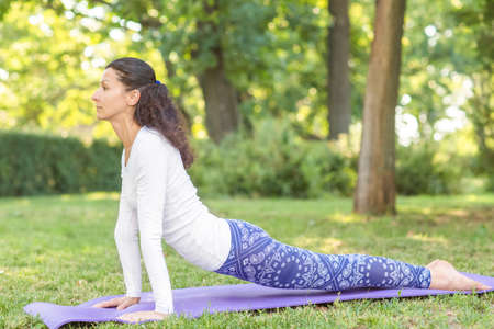 A balanced attractive girl working out in a park. Healthy girl on a purple mat in a sunny garden. Young woman exercising in the morning. Relaxing yoga positions.の写真素材