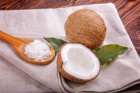 Close-up coconuts on a gray piece of cloth on a dark wooden background. Bright cut coco and green leafs. Delicious coconuts on a brown table. Spoon filled with white coconut flakes.の写真素材