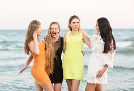 Attractive, good-looking and funny girls with pretty long hair and in multi-colored, fashionable and modern dresses, look happy on the sea beach background. Beautiful ladies on the beach.の写真素材