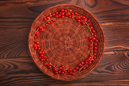 A colorful composition of a brown basket with juicy red currant on a dark wooden table. Fresh,mature, healthy and ripe red currant are lying inside, forming a good circle.の写真素材