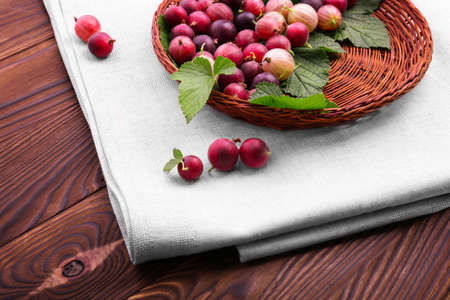 Close-up healthy multi-colored berries on a bright brown background. Gooseberries different shades of bright red color. An eco-friendly wooden basket on a table with fresh berries.の写真素材