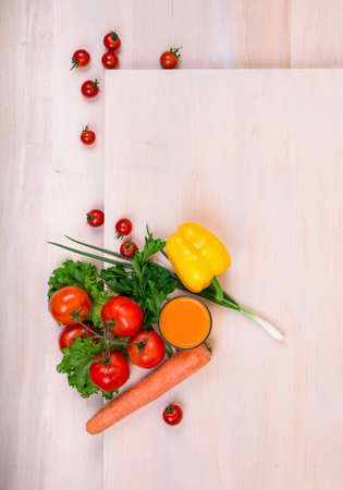 Tomatoes on a light brown wooden background. A variety of tasty and healthful vegetables: carrot, tomatoes, salad pepper, onions on a table.  A fresh orange juice near vegetables. Food ingredients.の写真素材