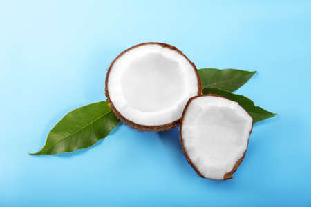 A close-up colorful cut coconuts on a bright light blue background. Coconut cracked into pieces and fresh leaves. Exotic fruits for vegan diet. Healthy lifestyle.の写真素材