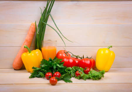 Colorful veggies on a bright light background. A rich assortment of nutritious vegetables. Fresh red tomatoes and a carrot. Rustic greens. Organic yellow pepper. Orange extract full of nutrients.の写真素材