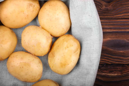 A large pile of nutritious and young potatoes in a gray bag on a dark brown wooden table. Organic and uncooked new light brown potatoes. Delicious and fresh vegetables.の写真素材