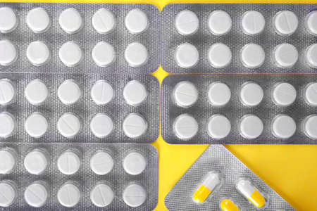 Close-up healthful vitamins in light gray blisters on a sunny yellow background. A view from above on a group if various medicaments: antibiotics, painkillers, drugs in white tablets.の写真素材