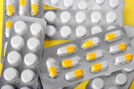 A close-up of various pills and drugs in gray packages on a bright yellow background. Prescripted narcotics and painkillers. White aspirin in tablets. Healthful lifestyle.の写真素材