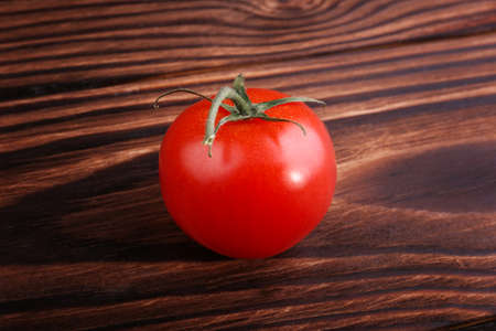 A single bright red tomato on a dark wooden background. Ripe veggie closeup. Delicious summer vegetables for the vegetarian diet. Freshness, organic, natural, juicy concept.の写真素材