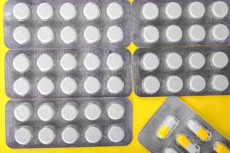 A top view of saturated gray packs with round white tablets on a shiny yellow background. Aspirin and painkillers in colorful capsules. Recovery, healing, therapy concept.の写真素材