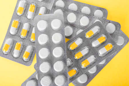 Various painkillers and antibiotics in shiny gray blisters on a yellow background. Orange and white prescripted narcotics. Tablets full of vitamins. Healthful pharmaceutical supplement.の写真素材