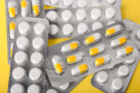Different pharmaceutical medicaments in brilliant packs on a spacious yellow background. Packs of orange and white antibiotics in organic capsules. Healthcare and medicine concept.の写真素材