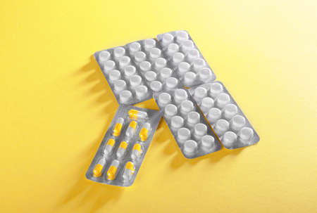 A top view of prescripted piles in round white tablets on a bright yellow background. A colorful close-up of different capsules in blisters. Drugs, antibiotics, painkillers to cure a sickness.の写真素材