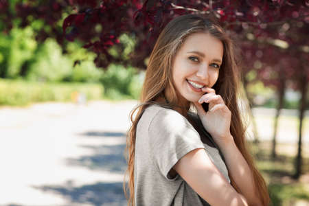 A smiling lady in a light shirt on a bright natural background. An adorable happy girl having fun in a sunny summer park. A gorgeous young woman laughing and posing. Healthy lifestyle.の写真素材
