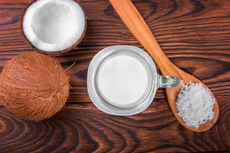 A mason jar full of fresh coco milk, a spoon with coconut chips and ripe coconuts on a dark brown wooden table.  Ripe, raw, fresh, healthy, organic and exotic nuts. Fresh and tasty coconut products.の写真素材