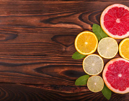A view from above on various citruses on a dark wooden background. Red grapefruits with a juicy texture. Sour yellow lemons and sweet oranges laying on a table. Tropical summer fruits.の写真素材