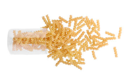 Delicious yellow macaroni isolated on a radiant white background. A transparent glass filled with uncooked spiral-shaped spaghetti. Mediterranean cuisine for vegetarians.の写真素材