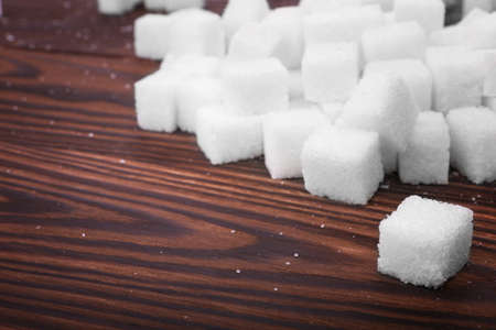 Many cubes of sweet sugar on a dark brown wooden table. White organic, refined sugar and sweet food...