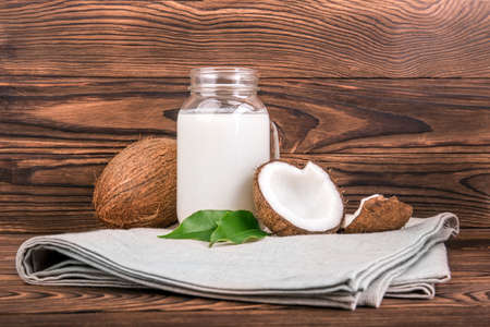 Coconuts with fresh green leaves and a mason jar of coconut milk on a light fabric and on a dark wooden background. Healthy food. Coconut and coconut milk in glass on wooden table. Tropical fruits.の写真素材