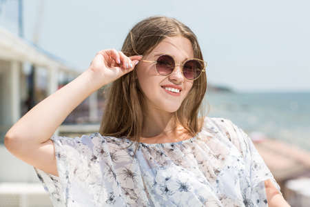 Beautiful and sweet girl in a light blouse with charming smiles against the sea background. Elegant, fashionable and beautiful girl with long, straight hair and in a light summer blouse, looks happy.の写真素材