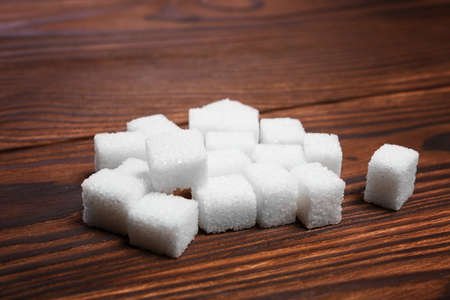 A heap of white pieces of sugar cubes for tea, coffee, baking and cooking on a wooden table. White crystals of sugar and sweet food ingredient on the table.の写真素材