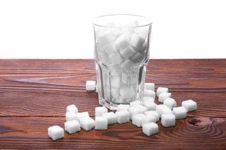 An entire glass of sweet sugar cubes on a table, isolated on a white background. White organic sugar on the dark brown wooden table. Consumption of bad calories.の写真素材