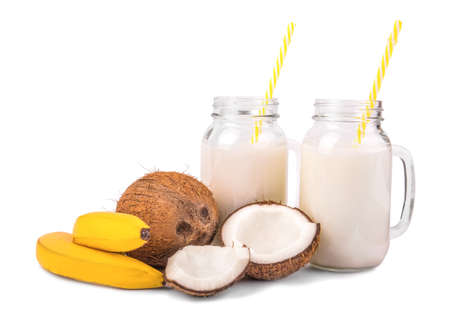 A composition of a whole and cut, fresh, organic coconuts, two tasty, sweetly bright yellow bananas and two mason jar full of natural, fresh coconut milk with yellow straws, isolated on a white background.の写真素材