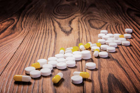 Close-up of different pills, tablets, vitamins, medicine, and drugs scattered on a dark wooden table. Pills for suicide. Treatment with pills and medicine.の写真素材