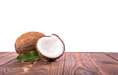 Tasty tropical coconuts with bright green leaves. Whole and cut natural, organic, fresh and tasty coconuts with green leaves on a wooden table, isolated on a white background.の写真素材